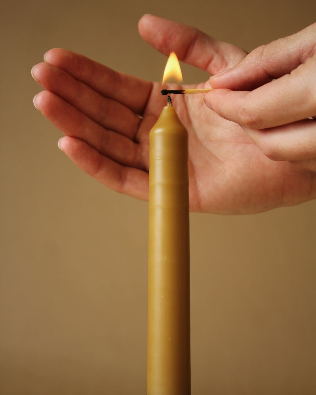 Hand lighting a yellow candle against a beige background